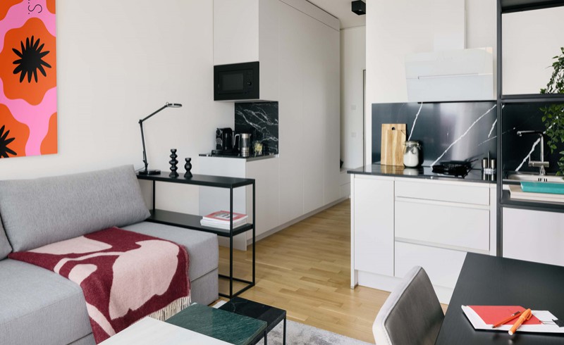 Coliving Apartment in Berlin mit grauem Sofa und bunter Tagesdecke sowie buntem Bild an der Wand 