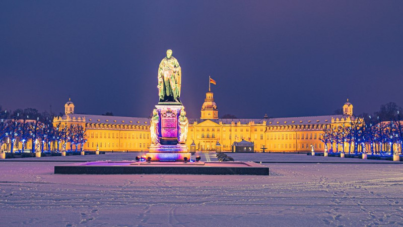 Beleuchtetes Schloss in Karlsruhe bei Nacht mit Schnee, im Vordergrund das Karl-Friedrich-Denkmal