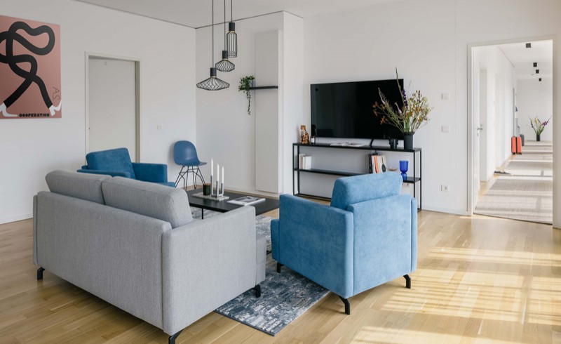 Coliving Wohnzimmer in Berlin mit grauem Sofa, blauem Sessel und modernem Flachbildschirmfernseher 