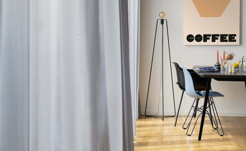 Coliving Wohnung in Berlin mit hellgrauen Vorhängen und modernem schwarzen Tisch und Stuhl