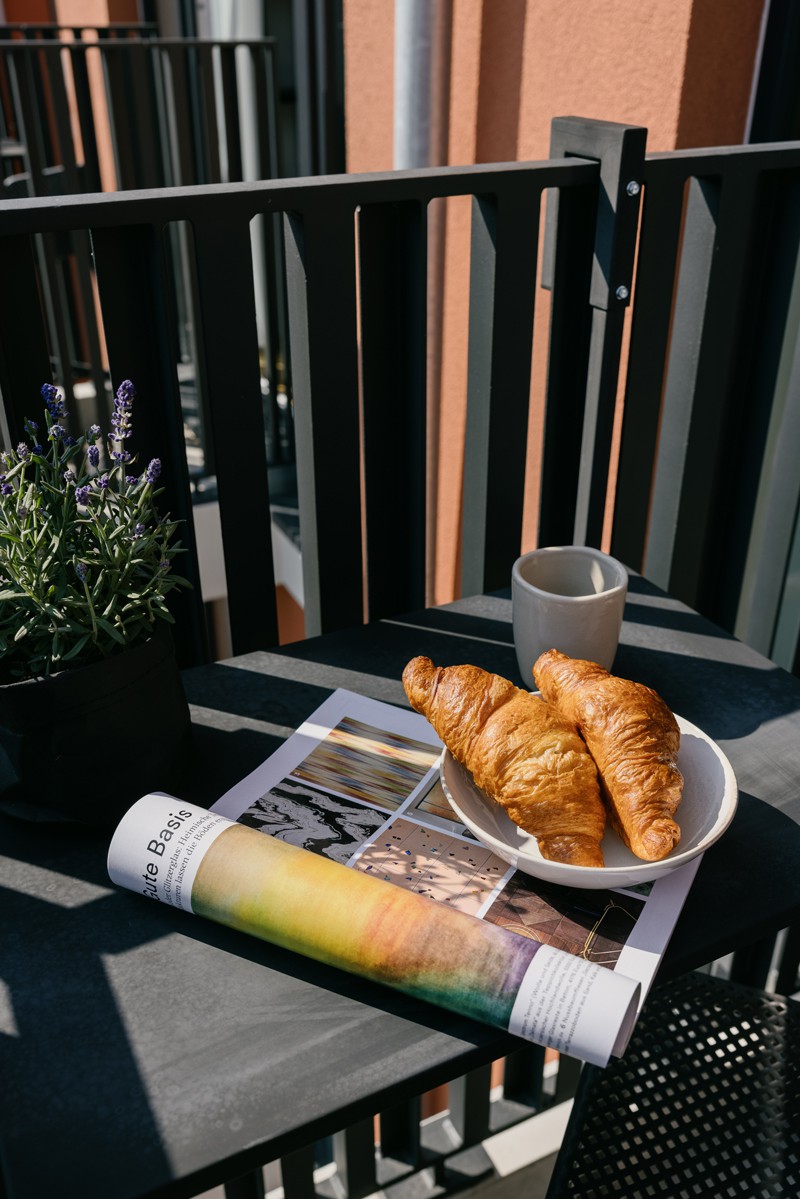 Balkon mit Tisch, auf dem eine Zeitschrift, ein Teller mit zwei Croissants und eine Tasse steht