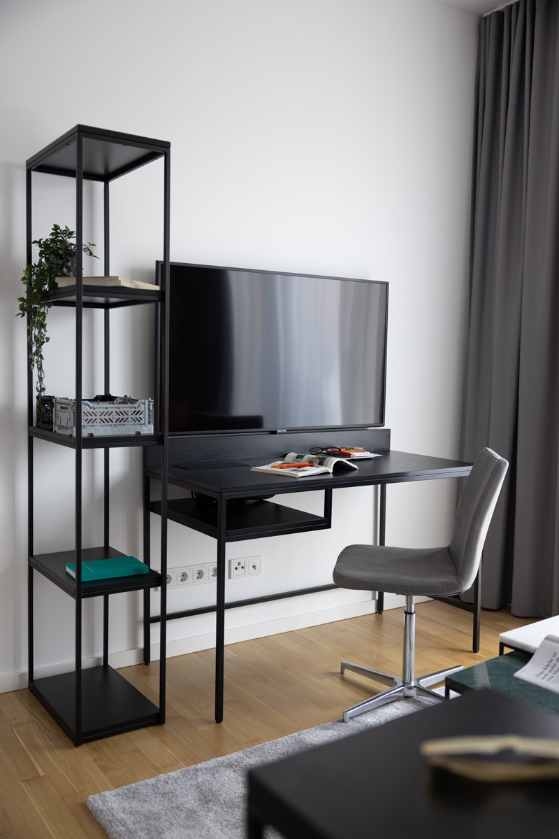 Micro apartment with a view of the desk, next to it a black shelf, above it the TV