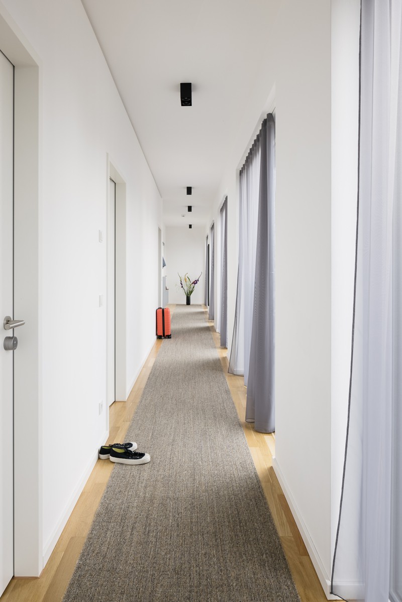 Light-flooded hallway of a House of Co coliving space, covered with gray carpet 