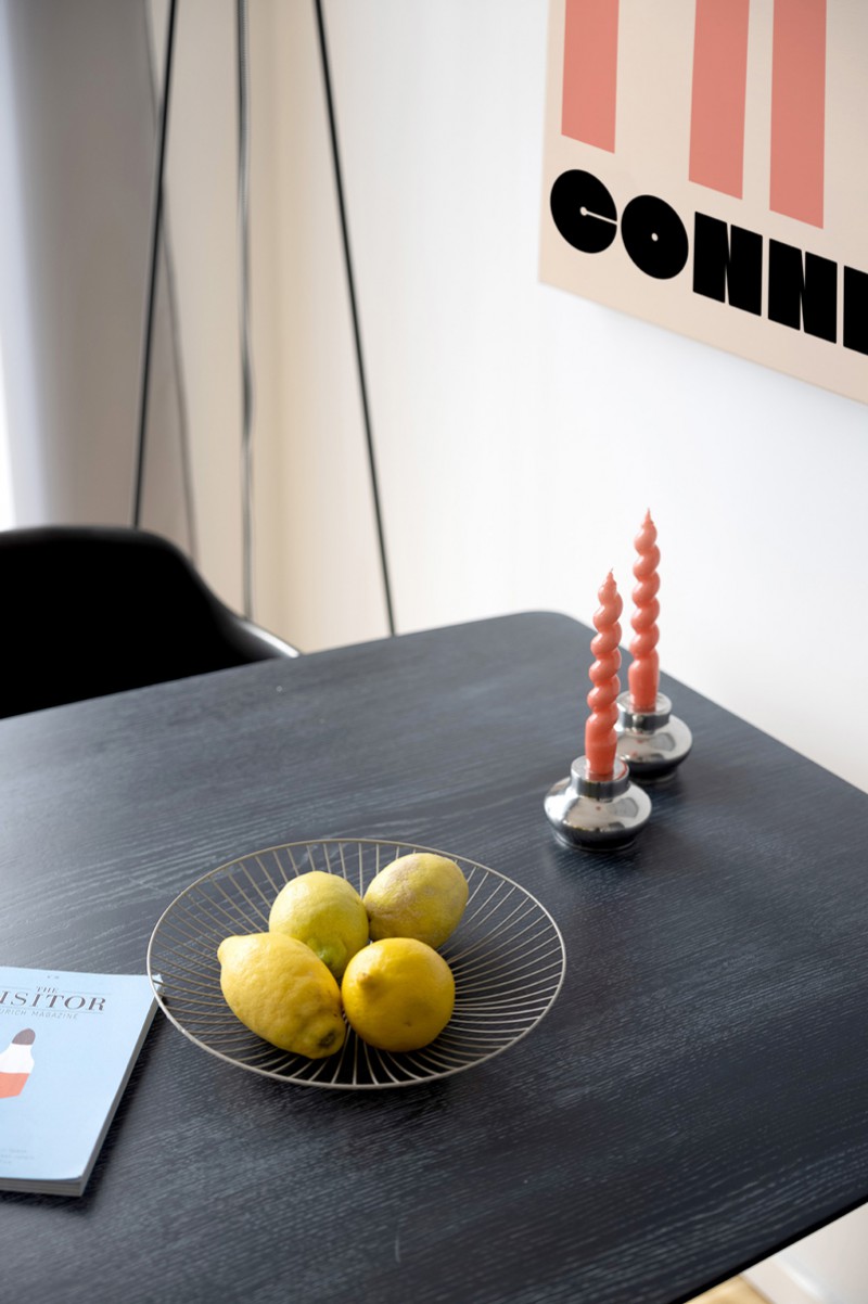 Black dining table on which there is a fruit bowl with lemons and two red candles