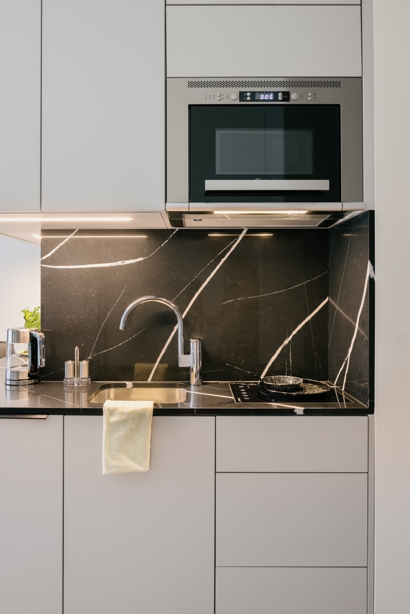 White kitchenette with black marble elements. In addition, a microwave above the sink