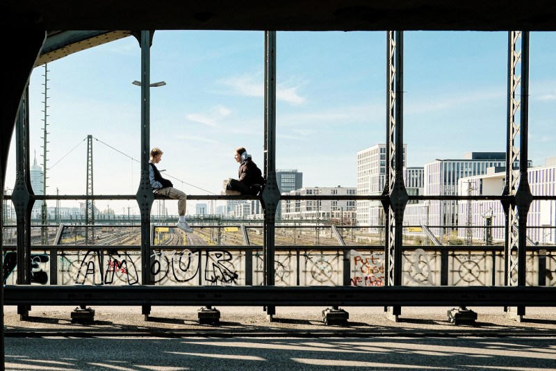 Zwei Personen sitzen auf dem Geländer der Hackerbrücke in München und genießen die Aussicht.
