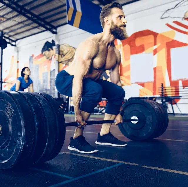 Muscular man performing a heavy deadlift in a gym with colorful graffiti on the walls.
