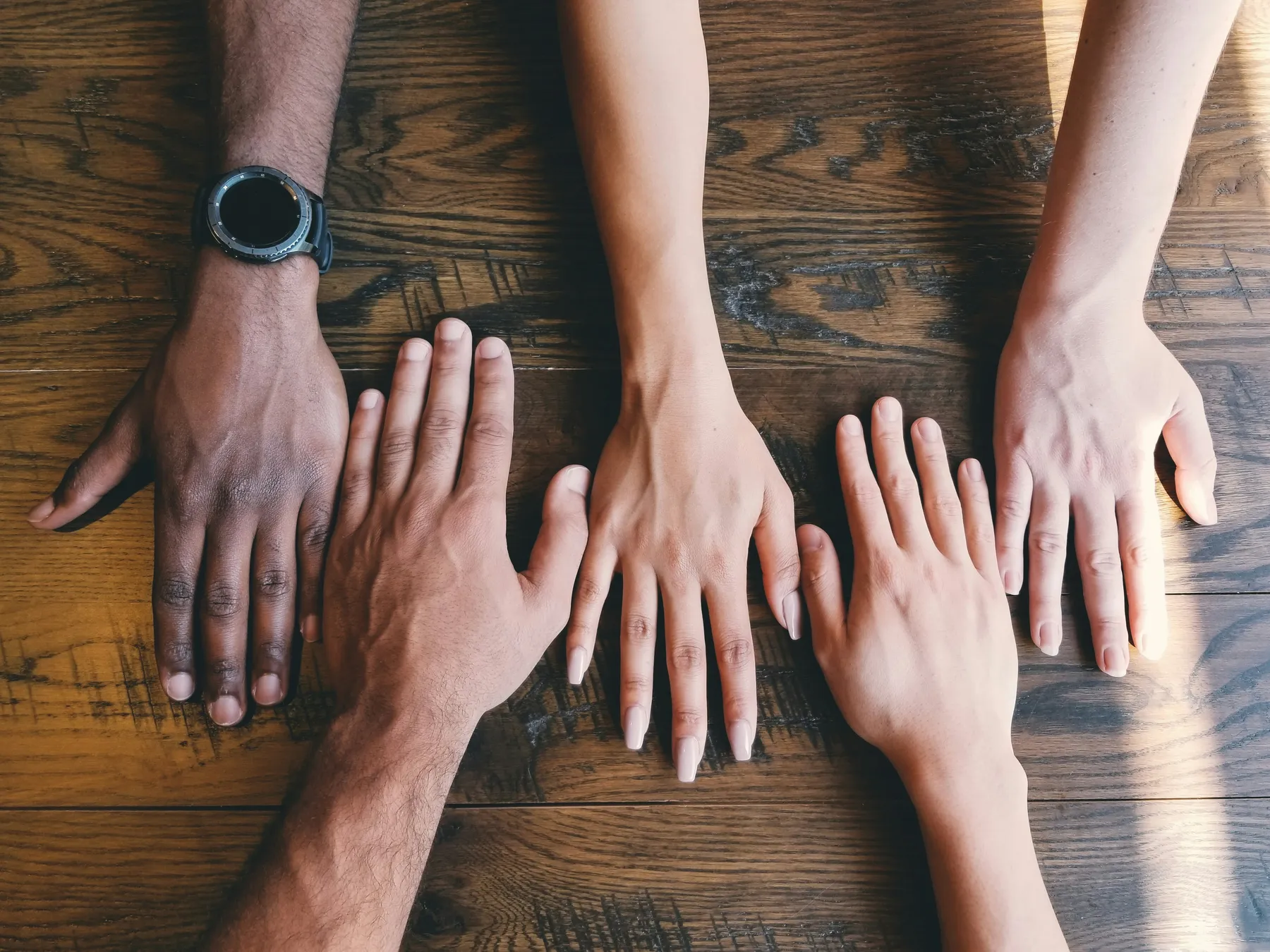 Five diverse hands placed together on a wooden table, symbolizing unity and teamwork.