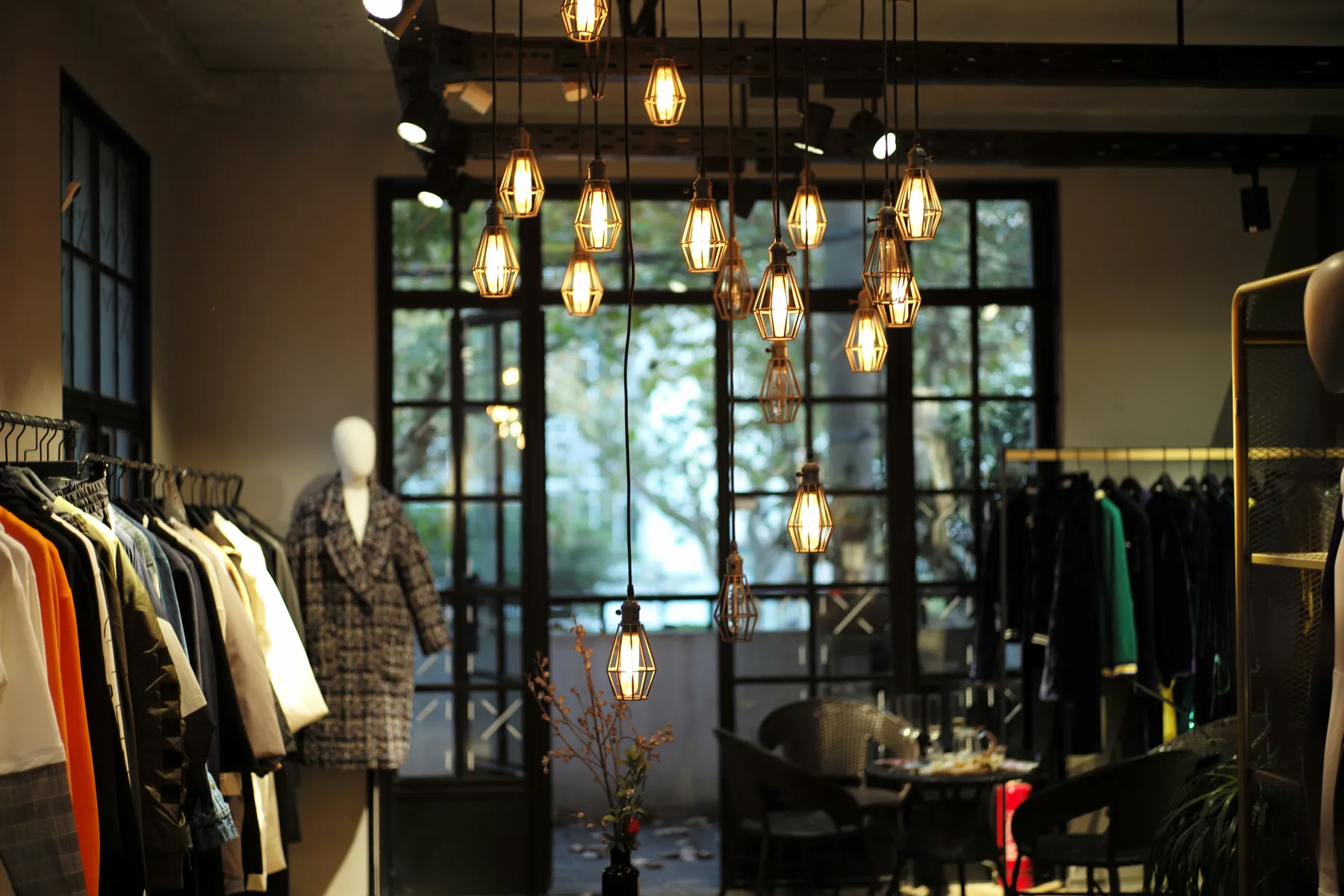 Stylish boutique interior with modern hanging lights, mannequins, and racks of fashionable clothing.